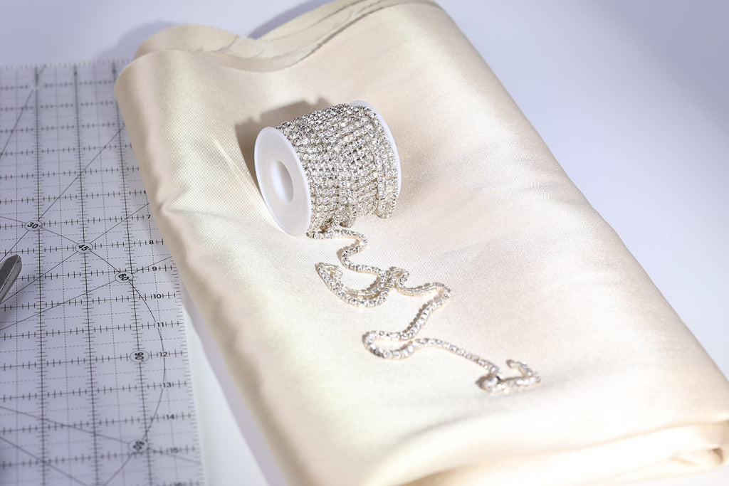 A spool of rhinestone-encrusted thread and a piece of fabric are placed on a white surface, with a ruler visible in the background.
