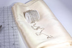 A spool of rhinestone-encrusted thread and a piece of fabric are placed on a white surface, with a ruler visible in the background.