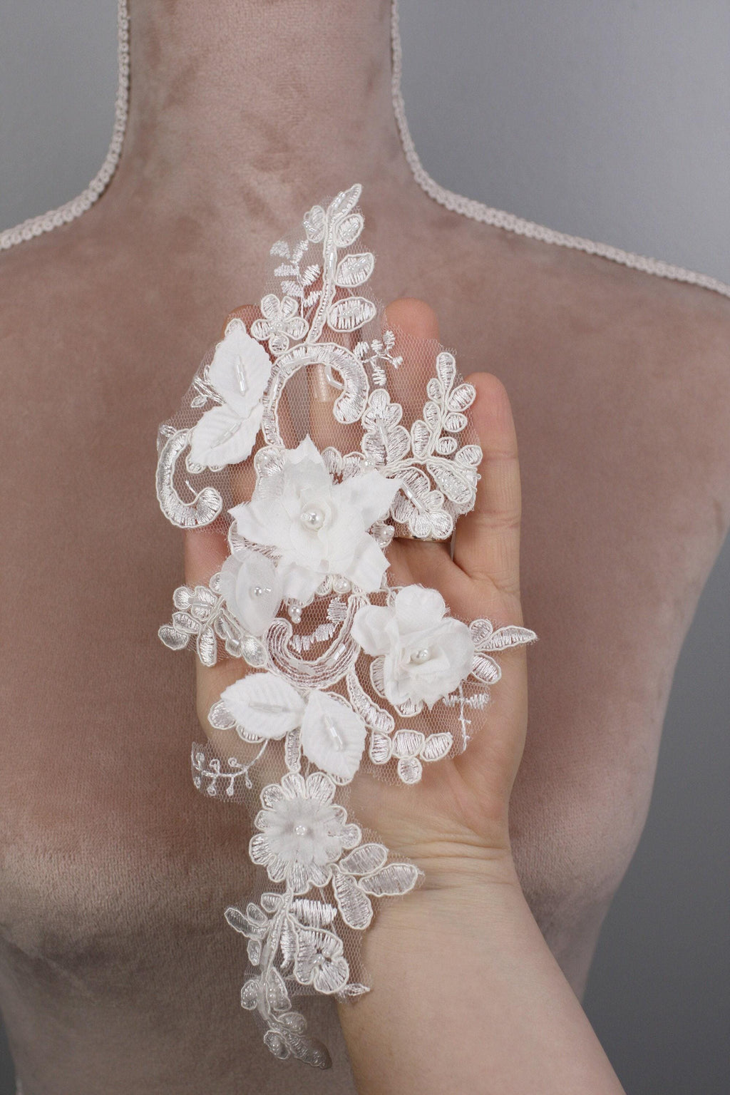 A hand holding a delicate, white lace flower attached to a mannequin torso.