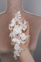 A hand holding a delicate, white lace flower attached to a mannequin torso.