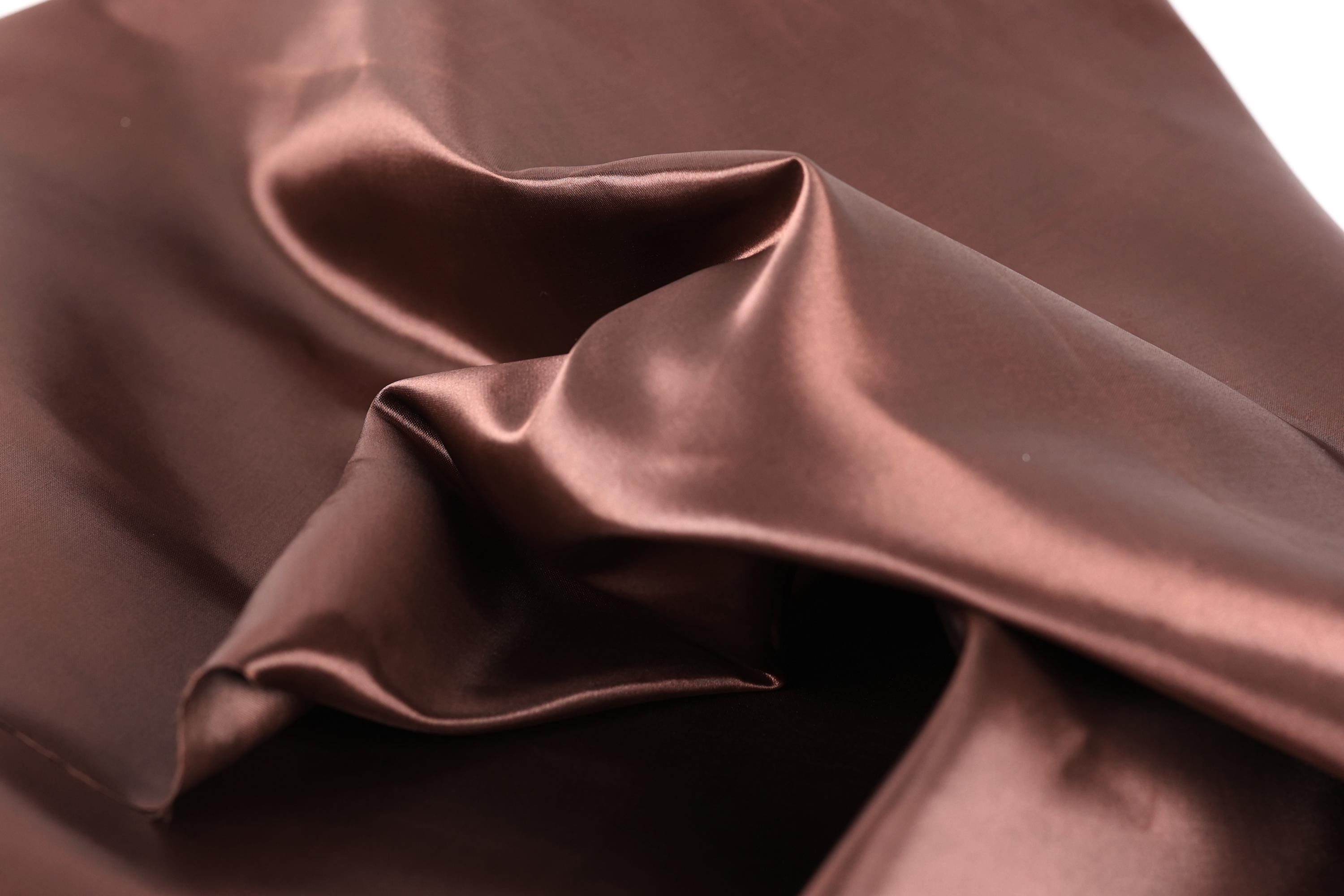 a close-up view of a crumpled, shiny brown fabric, possibly silk or satin, with a smooth, shiny texture.