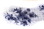 a close-up view of a delicate, intricate floral embroidery design. The design is composed of numerous small blue flowers and leaves, arranged in a visually appealing manner. The flowers are intricately detailed, showcasing the craftsmanship involved in creating this piece of art. The image does not contain any text or other discernible objects, and the focus is solely on the floral design.