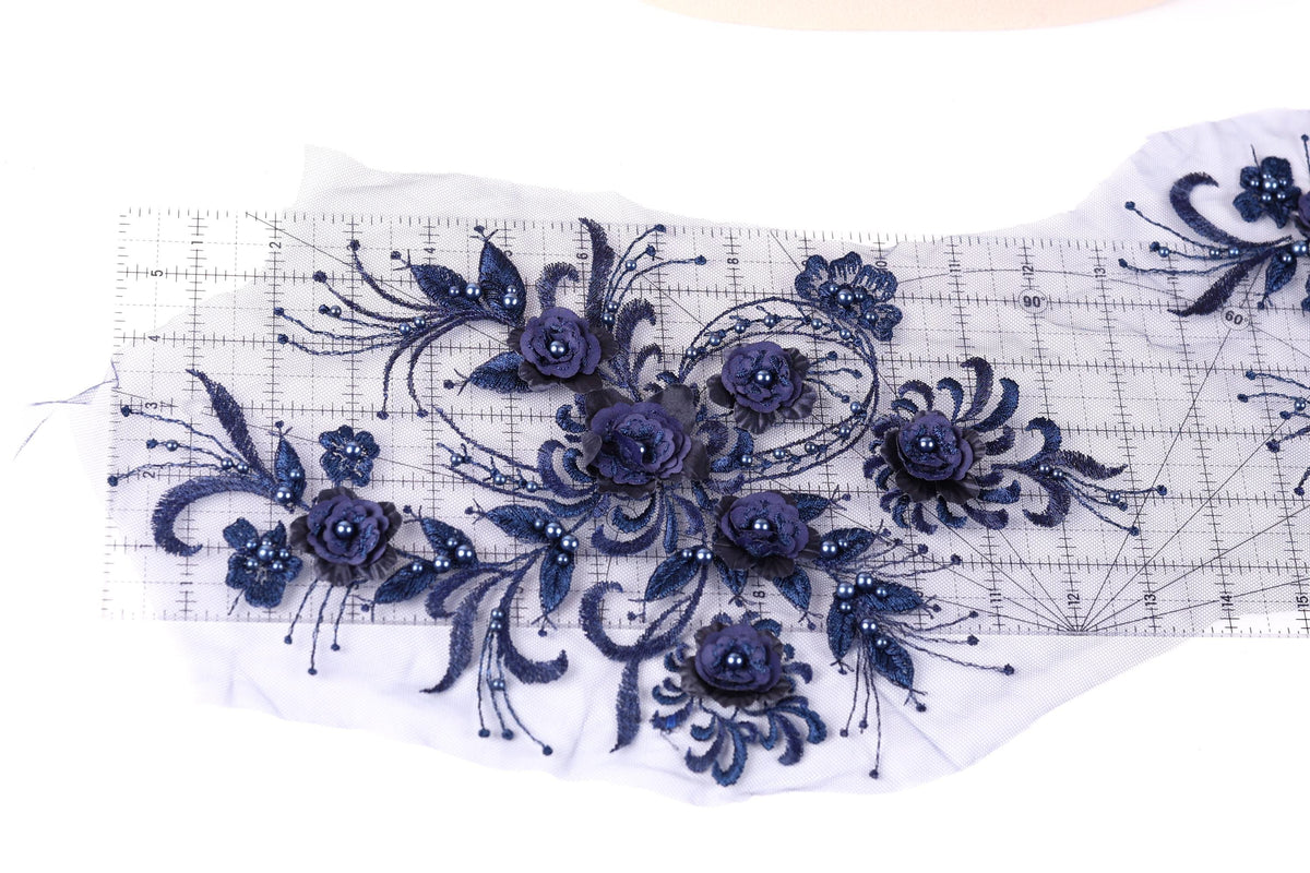a close-up view of a delicate, intricate floral embroidery design. The design is composed of numerous small blue flowers and leaves, arranged in a visually appealing manner. The flowers are intricately detailed, showcasing the craftsmanship involved in creating this piece of art. The image does not contain any text or other discernible objects, and the focus is solely on the floral design.