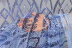A hand is holding a piece of blue fabric with sequin details, against a background of similar blue and white sequin patterns.