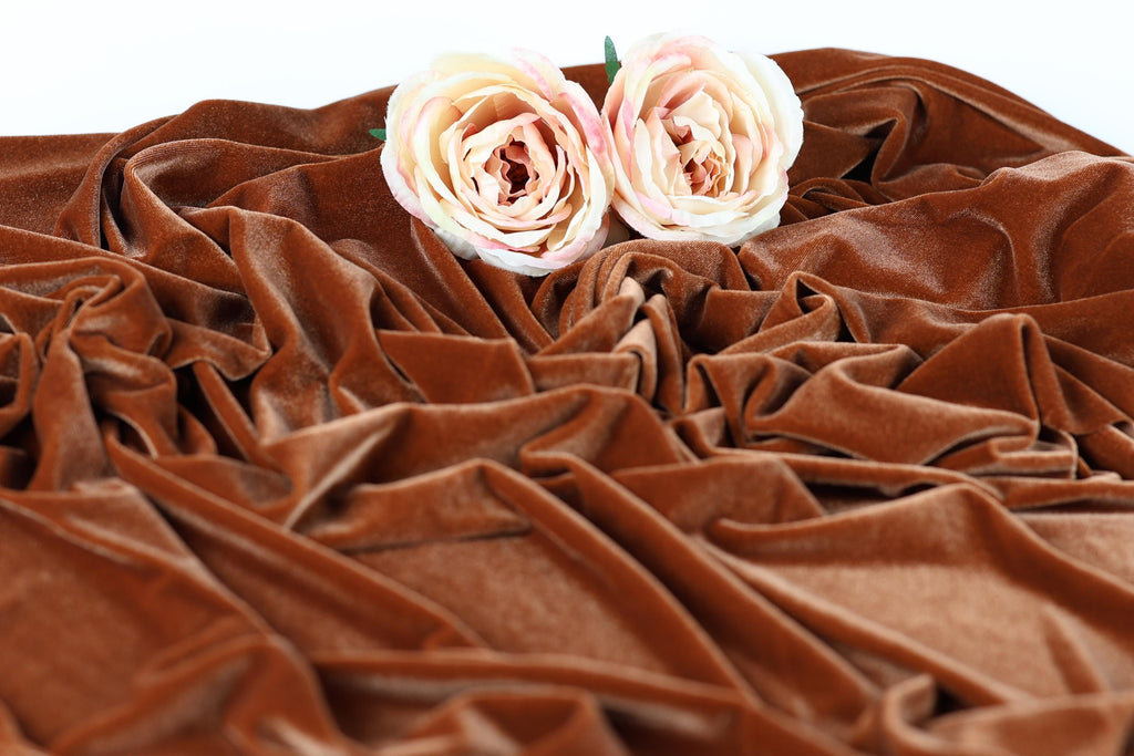 Two white roses with green leaves are placed on a crumpled brown fabric.