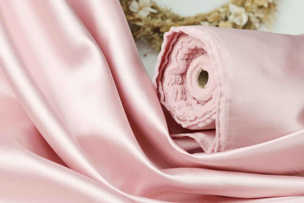 A close-up view of a soft, pink satin fabric, possibly silk, with a rolled-up end visible.