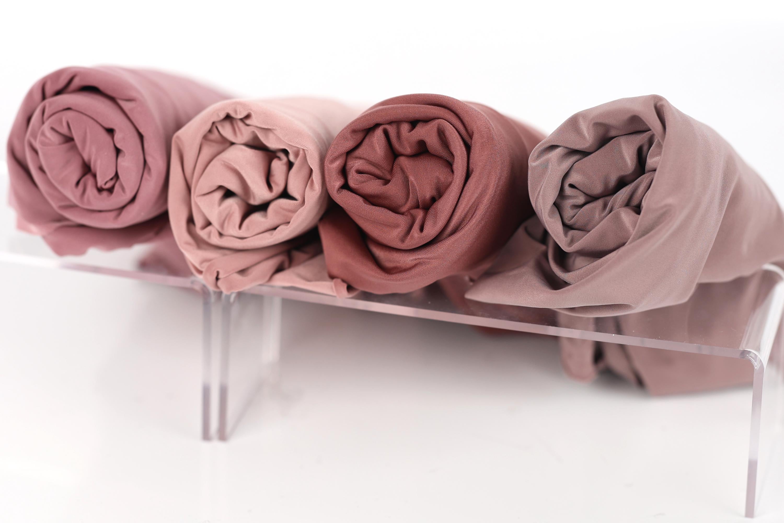 four rolled-up fabric pieces in different shades of pink, arranged on a clear stand.