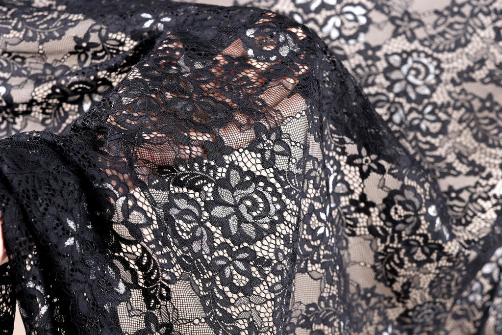 a close-up view of a black lace fabric with intricate floral patterns. The fabric appears to be made of sheer material, giving it a delicate and elegant appearance.