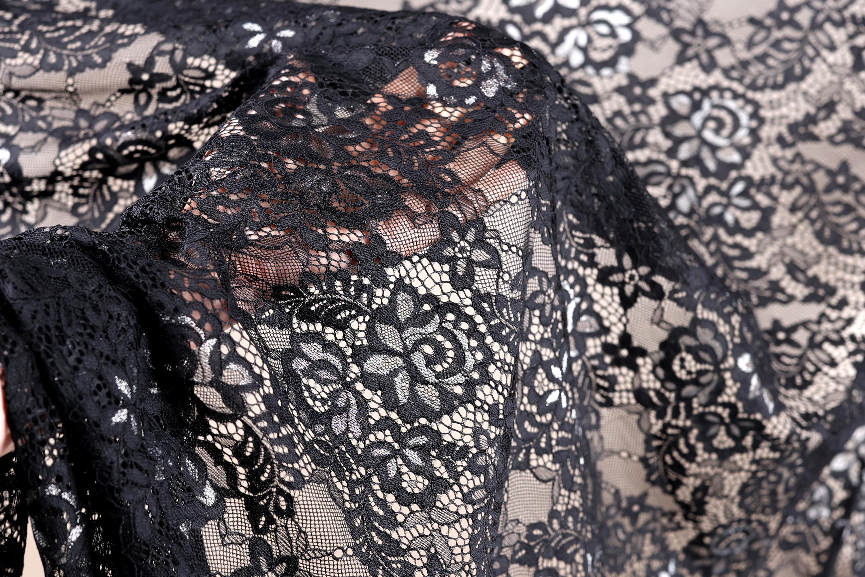 a close-up view of a black lace fabric with intricate floral patterns. The fabric appears to be made of sheer material, giving it a delicate and elegant appearance.