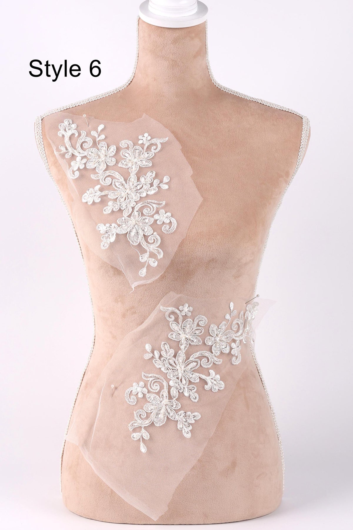 A mannequin with a beige body and a white head, wearing a white lace dress with floral embroidery.