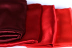 a close-up view of a collection of red and burgundy-colored fabric pieces, possibly silk or satin, arranged in a row.