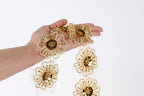 A hand holding a chain of gold-colored, intricately designed flower-shaped embellishments.