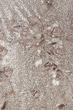 The image is a close-up of a fabric with a floral pattern, featuring a variety of flowers and leaves in shades of brown and beige. The pattern is intricate and detailed, with the flowers and leaves appearing to be made of sequins or other embellishments. The overall composition of the image is visually appealing and showcases the craftsmanship of the fabric design.