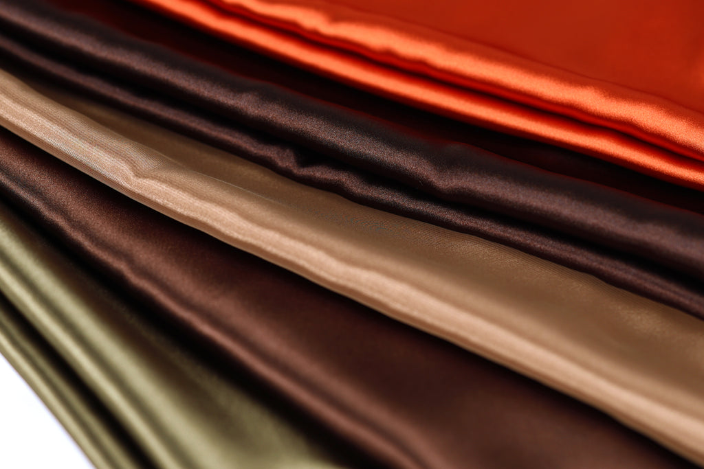 A close-up image of various colored satin fabric, including shades of brown, orange, and green, arranged in a visually appealing manner.