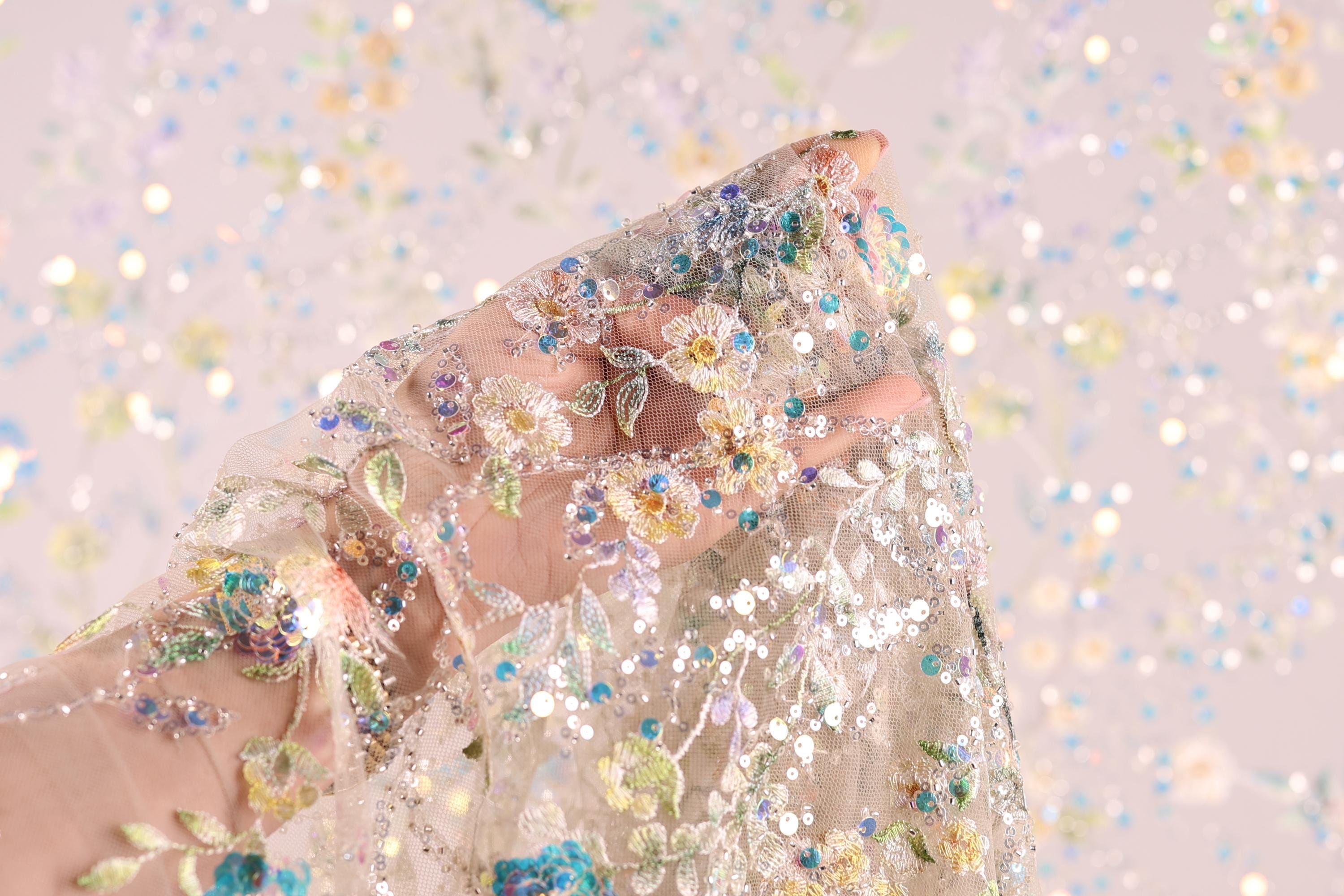 A hand is holding a delicate, intricately embroidered fabric with a floral pattern.