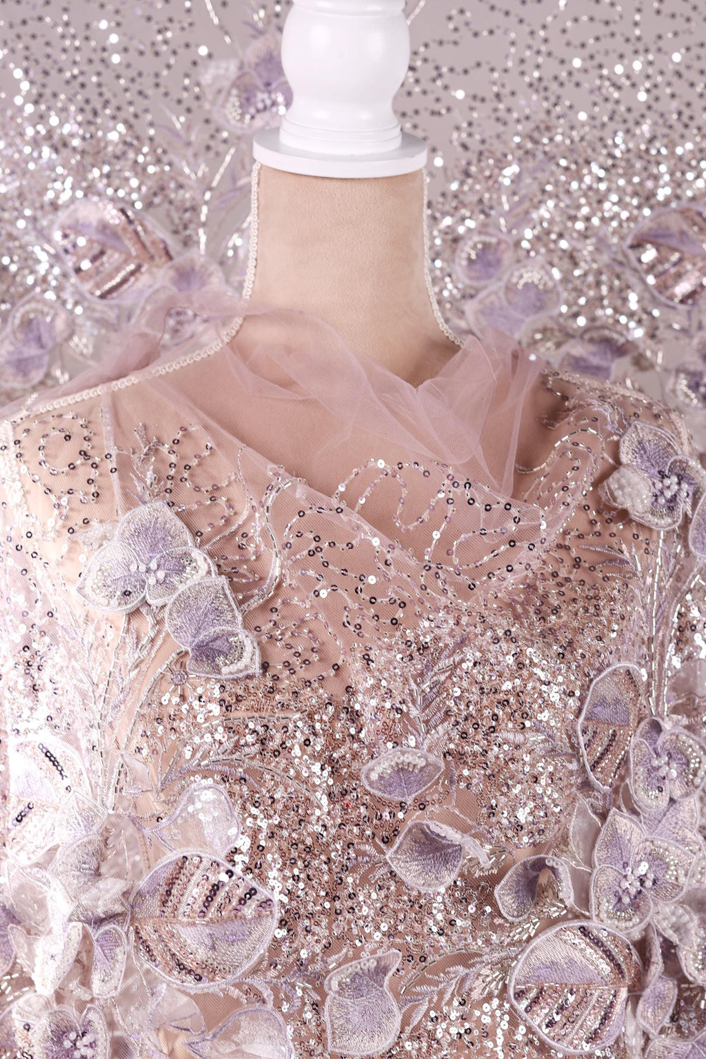 a mannequin wearing a dress with a pink and white floral pattern, as well as sequins and lace details.
