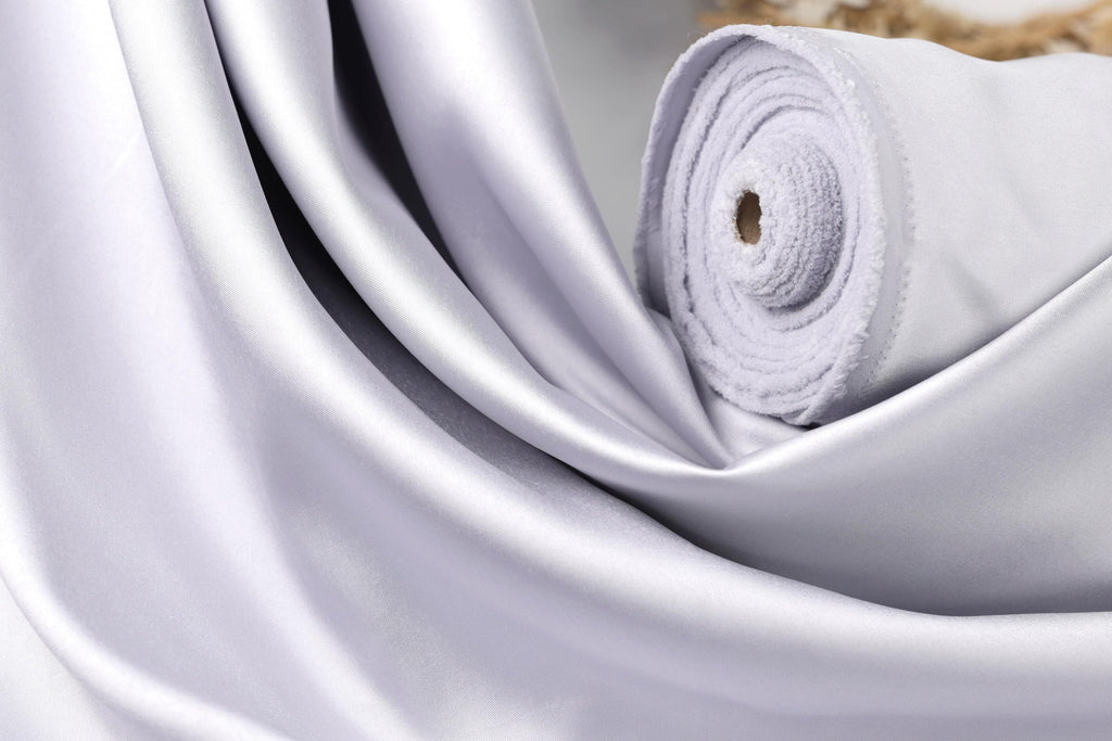 A close-up view of a white satin fabric, possibly silk, with a smooth and shiny texture.