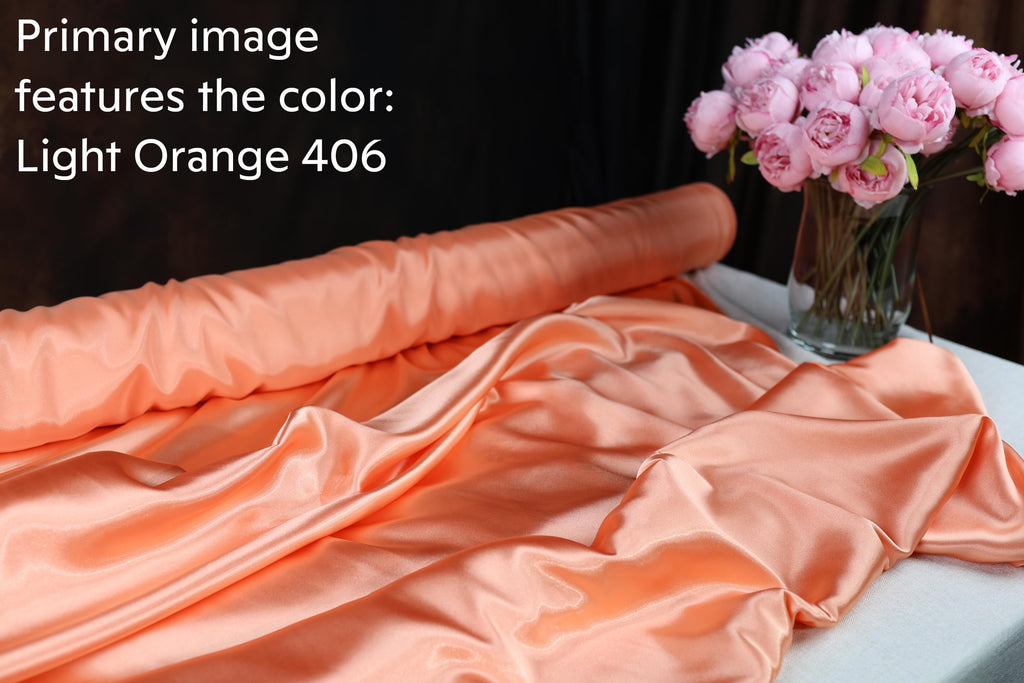 a roll of light orange fabric and a vase of pink flowers on a table.