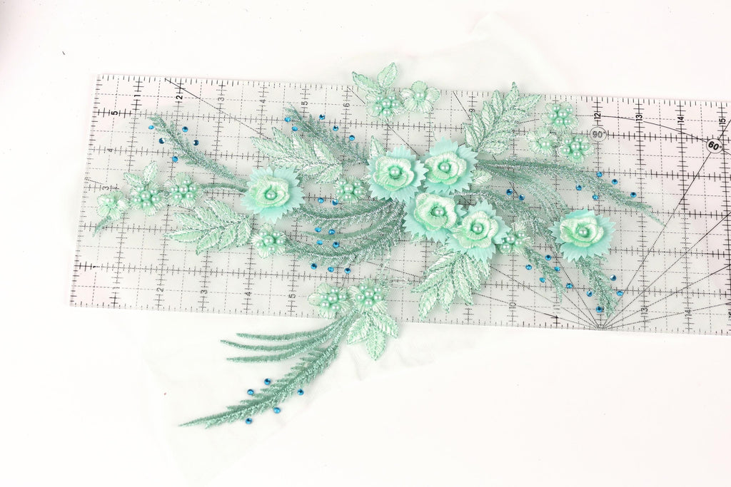 a collection of green floral embroidery pieces, including flowers and leaves, arranged on a transparent ruler.