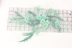 a collection of green floral embroidery pieces, including flowers and leaves, arranged on a transparent ruler.