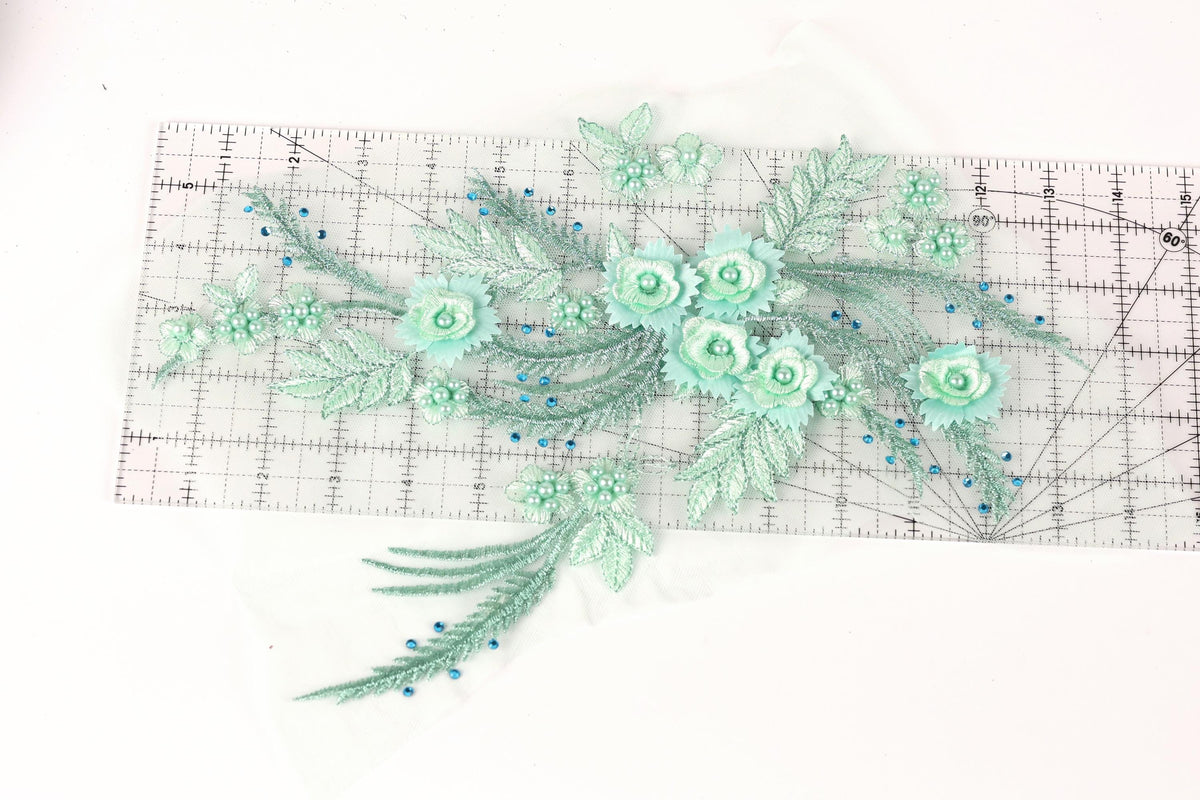 a collection of green floral embroidery pieces, including flowers and leaves, arranged on a transparent ruler.