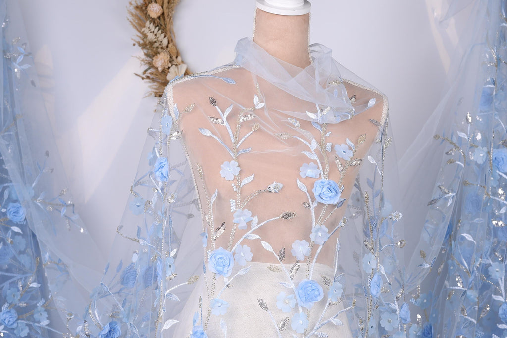 A mannequin wearing a white dress with a sheer blue floral fabric draped over it.