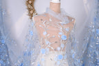 A mannequin wearing a white dress with a sheer blue floral fabric draped over it.