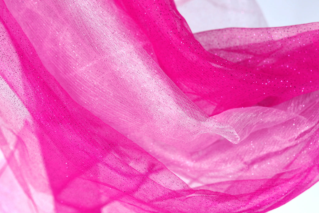 The image is a close-up of a fabric with a pink and white color scheme, featuring a shiny, sparkly texture.