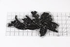 a close-up view of a black, intricate piece of embroidery or beading, with a ruler placed on top of it to measure its dimensions.