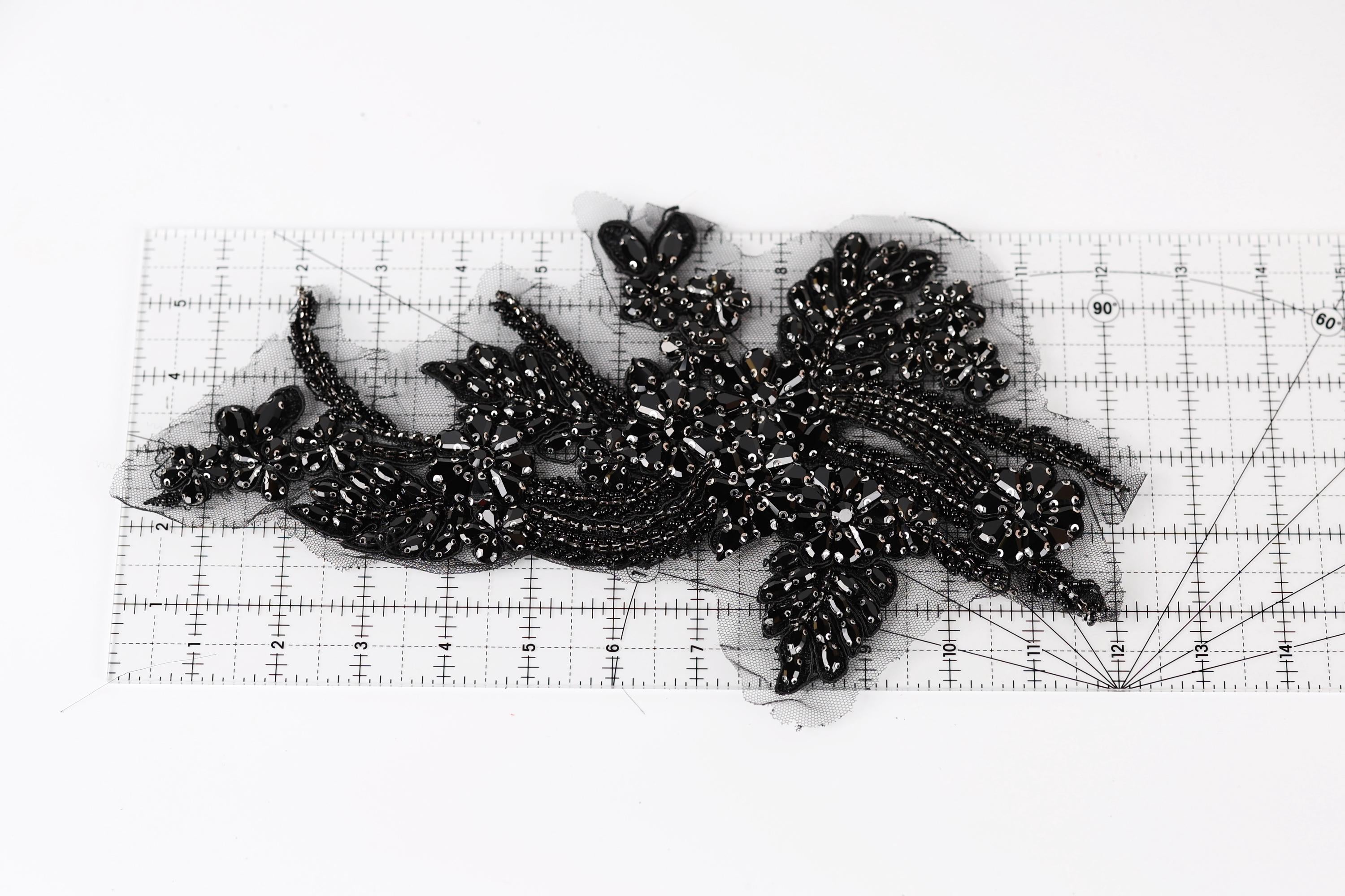 a close-up view of a black, intricate piece of embroidery or beading, with a ruler placed on top of it to measure its dimensions.