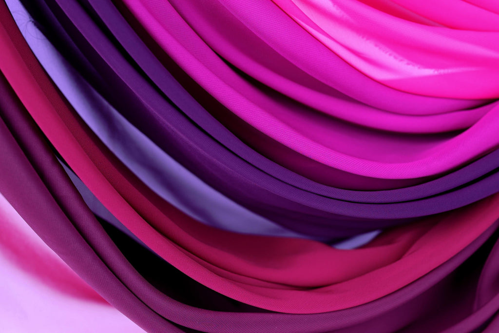 a close-up view of a variety of colorful fabrics, including shades of pink, purple, and blue. The fabrics are arranged in a visually striking and vibrant manner, creating a sense of depth and texture.