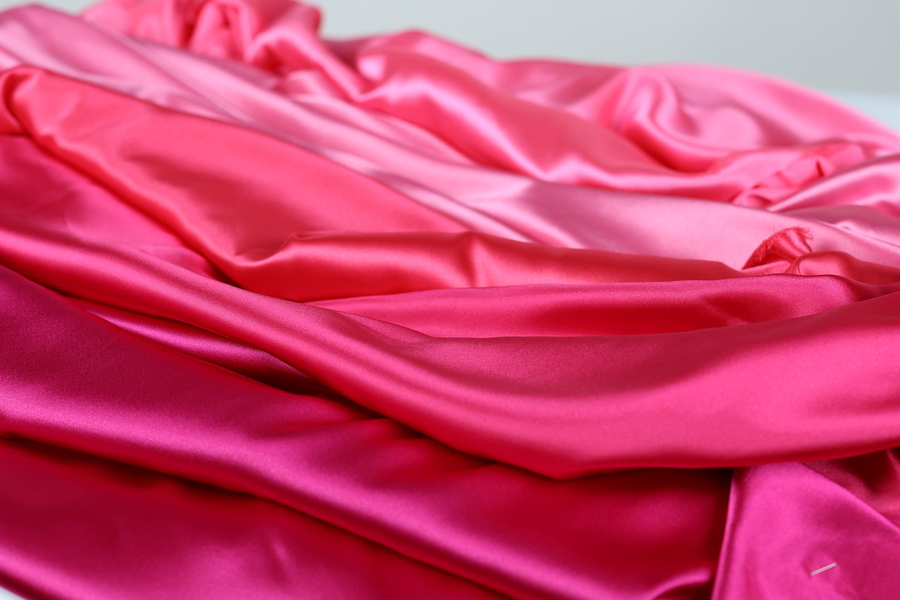 a close-up view of a pile of pink satin fabric, with varying shades of pink visible.
