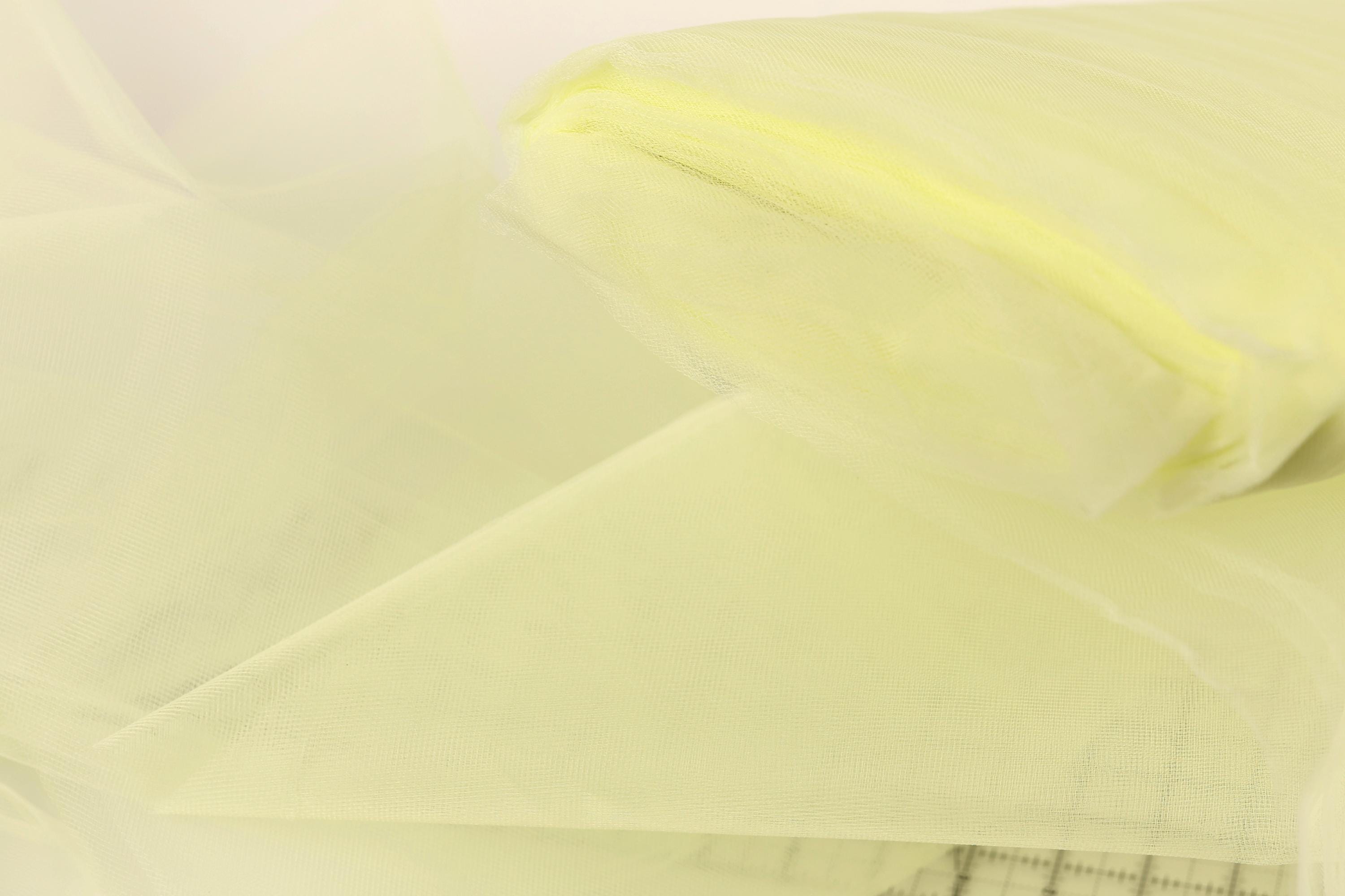 The image is a close-up of a yellow fabric, possibly tulle, with a textured appearance.