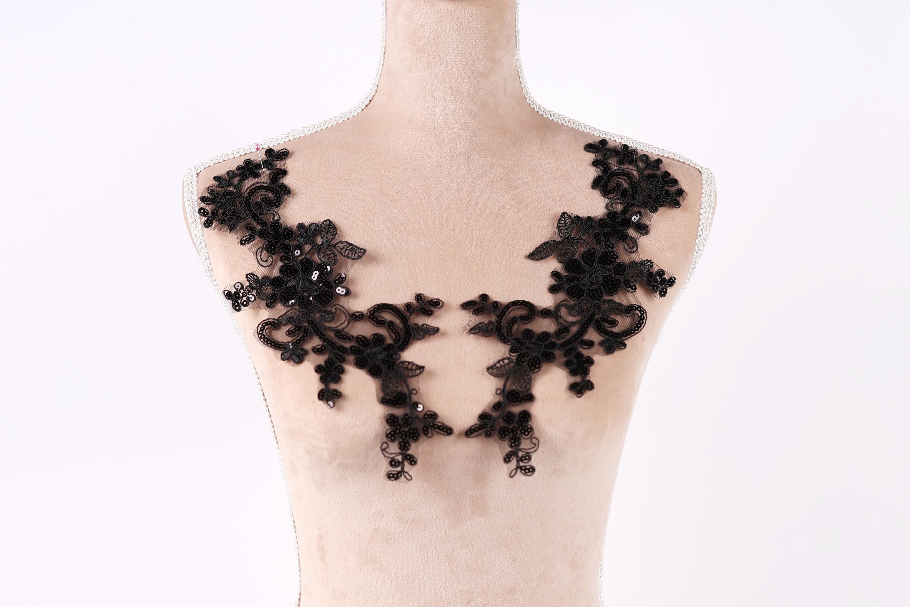 A mannequin wearing a black lace dress with intricate floral patterns.