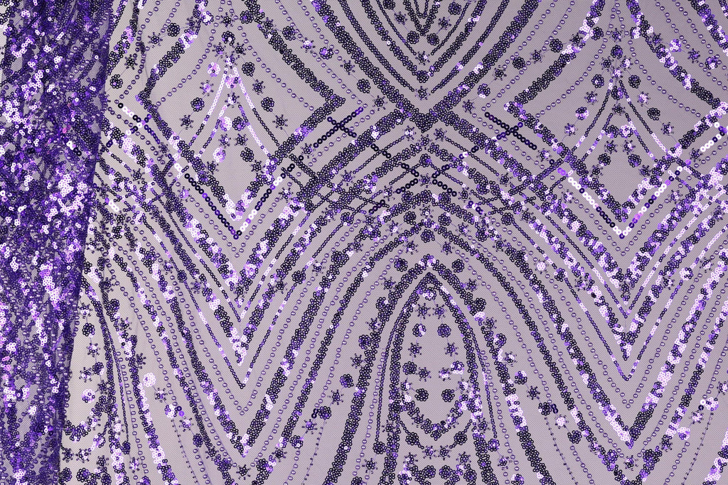 a close-up view of a fabric with a purple and black pattern, including a repeating diamond-shaped motif and a zigzag pattern. The fabric appears to be made of sequins or beads, creating a visually striking and intricate design.