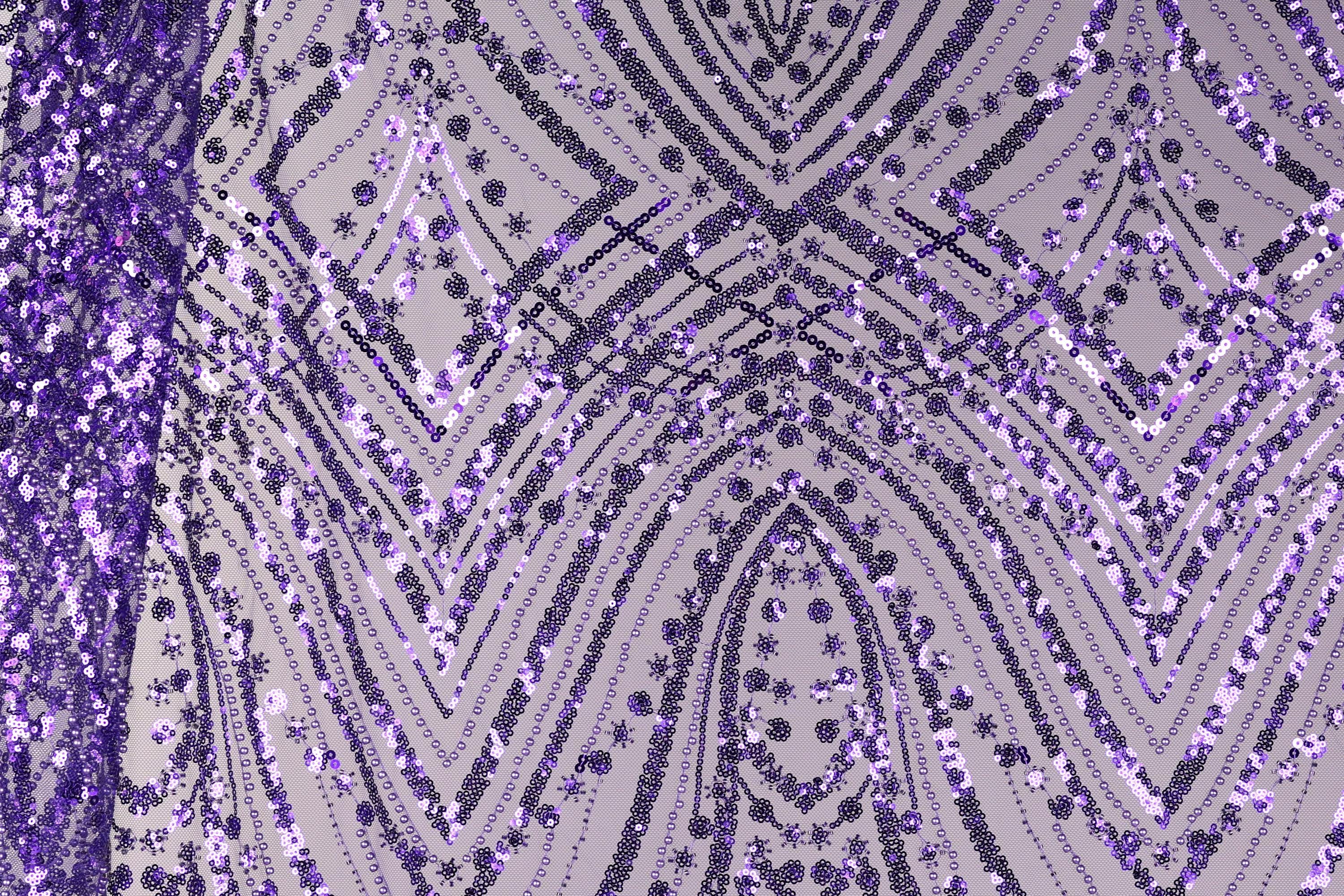 a close-up view of a fabric with a purple and black pattern, including a repeating diamond-shaped motif and a zigzag pattern. The fabric appears to be made of sequins or beads, creating a visually striking and intricate design.