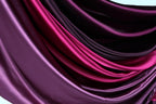 a close-up view of a fabric with a gradient of colors, transitioning from a deep purple to a lighter shade of purple. The fabric appears to be made of satin or a similar smooth, shiny material, and it is folded or draped in a way that creates a sense of depth and texture.