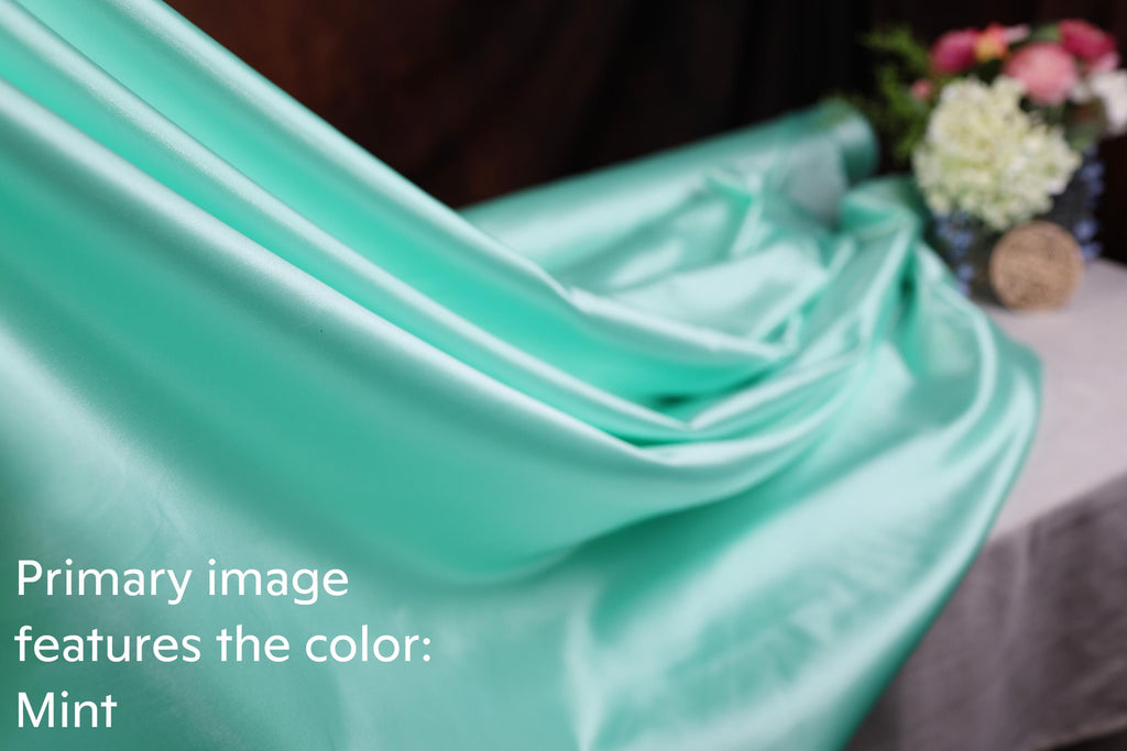 A close-up view of a mint-colored fabric, with a blurred background featuring a vase of flowers.