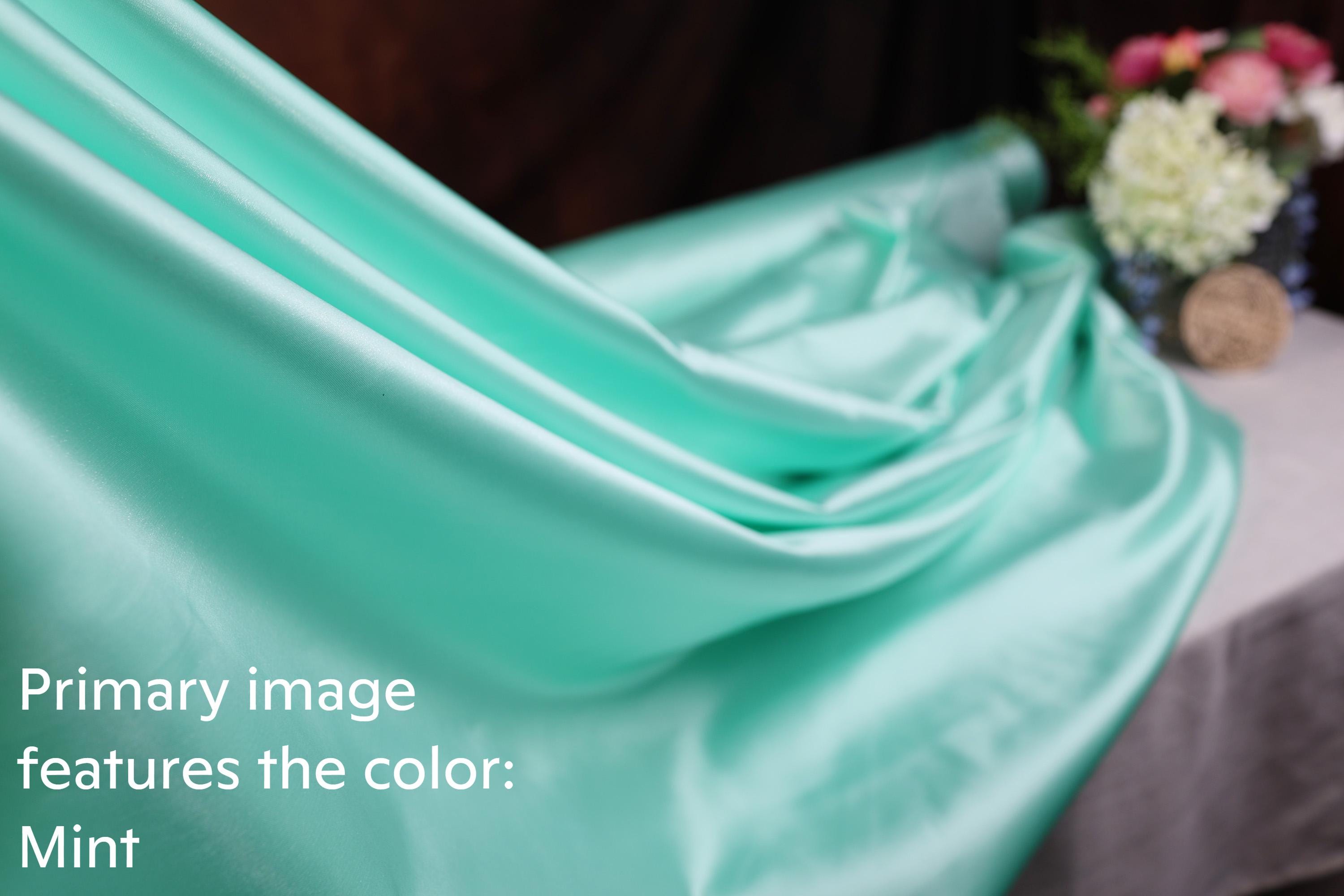A close-up view of a mint-colored fabric, with a blurred background featuring a vase of flowers.