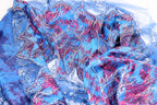 a close-up view of a fabric with a vibrant, colorful pattern of blue, red, and silver sequins or beads. The fabric appears to be a type of lace or sheer material, with a textured and intricate design.