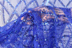 A close-up view of a hand holding a piece of blue sequin fabric.