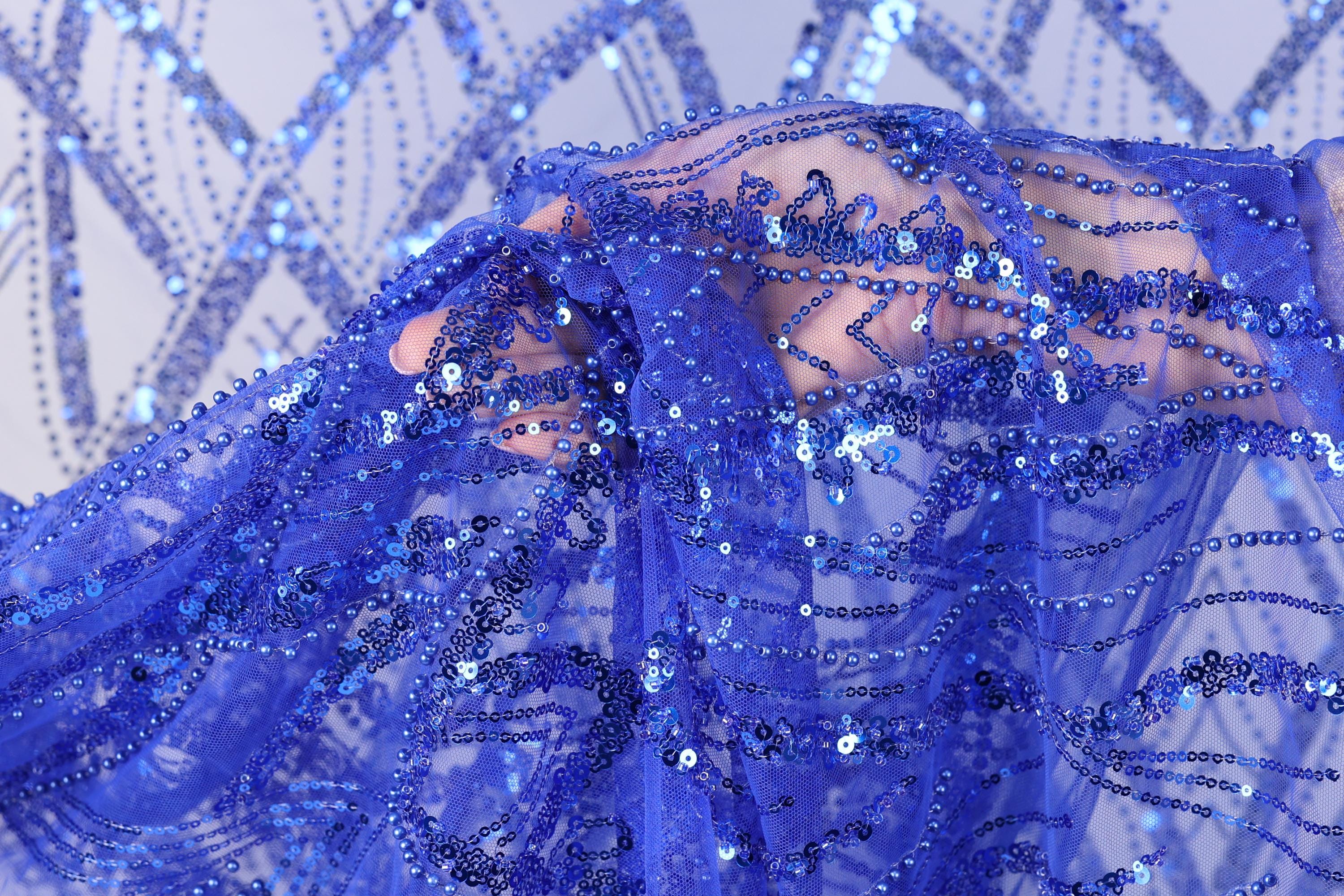 A close-up view of a hand holding a piece of blue sequin fabric.