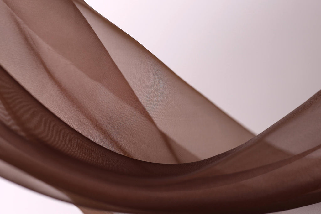 a close-up view of a brown fabric, possibly a piece of clothing or a textile, with a soft, flowing texture. The fabric appears to be made of a soft, shiny material, and it is draped or draped over a surface, creating a sense of movement and softness.