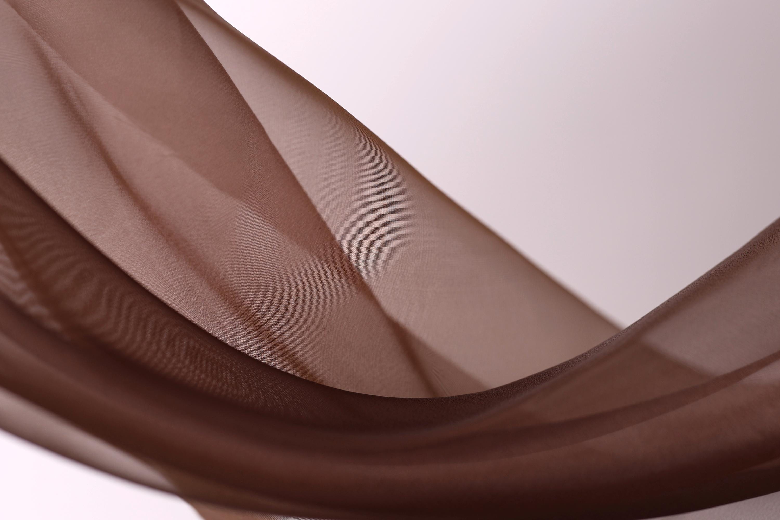 a close-up view of a brown fabric, possibly a piece of clothing or a textile, with a soft, flowing texture. The fabric appears to be made of a soft, shiny material, and it is draped or draped over a surface, creating a sense of movement and softness.