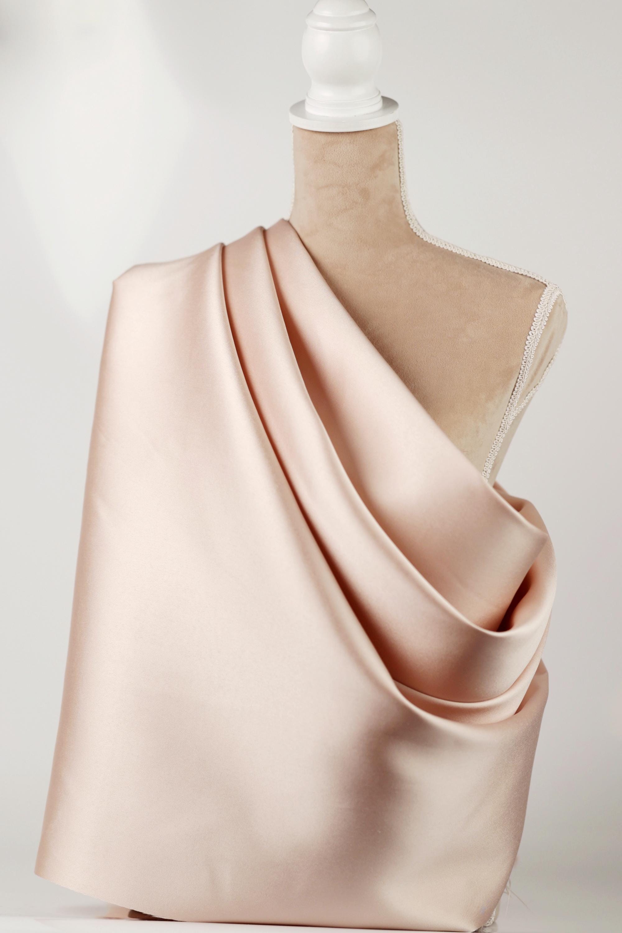 A mannequin wearing a pink satin fabric draped over its shoulder.