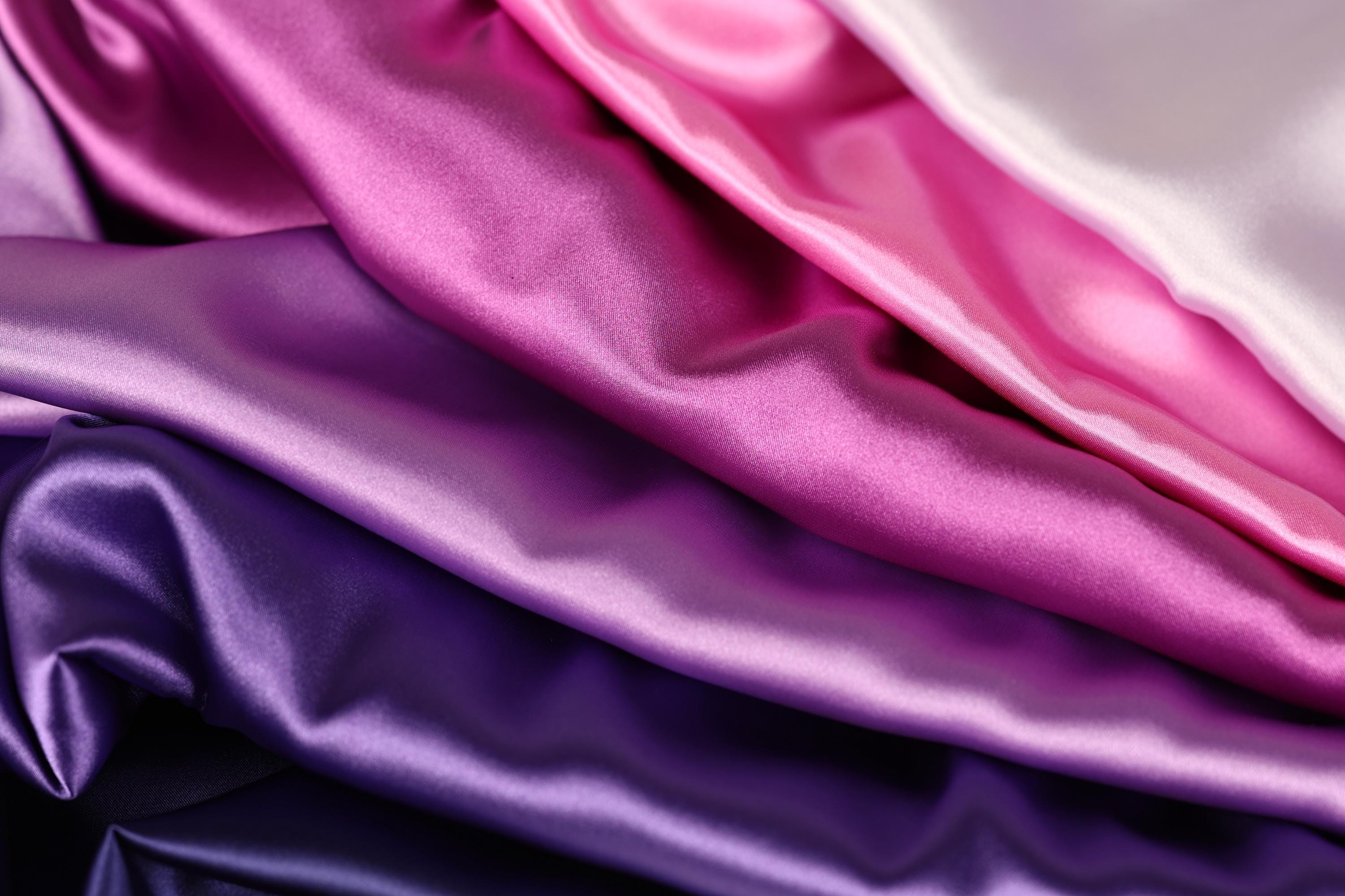 a close-up view of a pile of colorful satin fabric, with shades of pink, purple, and blue.