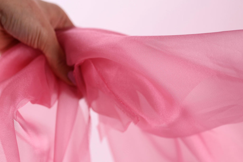 A hand is holding a pink fabric, which appears to be a soft, flowing material.