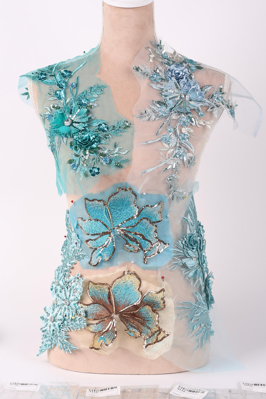 a dress with intricate blue and green floral embroidery, including various types of flowers and leaves. The dress appears to be a part of a collection or a fashion design, showcasing the craftsmanship and attention to detail in the embroidery work.