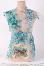 a dress with intricate blue and green floral embroidery, including various types of flowers and leaves. The dress appears to be a part of a collection or a fashion design, showcasing the craftsmanship and attention to detail in the embroidery work.