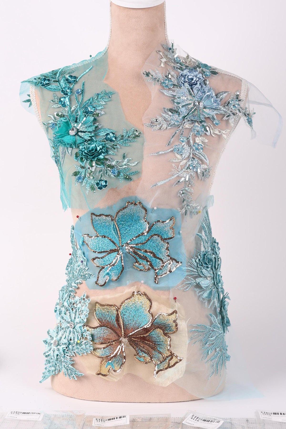 a dress with intricate blue and green floral embroidery, including various types of flowers and leaves. The dress appears to be a part of a collection or a fashion design, showcasing the craftsmanship and attention to detail in the embroidery work.